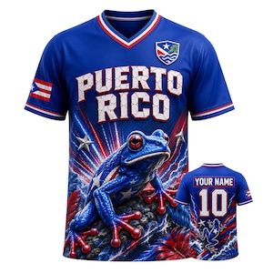 Puede incluir: Una camiseta azul con cuello en V que presenta el texto PUERTO RICO, un gráfico de una rana azul y un emblema. La manga muestra la bandera de Puerto Rico. La parte trasera incluye el texto YOUR NAME, el número 10 y una rana pequeña.