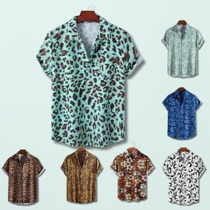 Puede incluir: Colección de camisas de manga corta con estampados variados. Las camisas, colgadas en perchas de madera, presentan estampados de leopardo, cebra y flores. La paleta de colores incluye marrón, azul, verde y blanco.