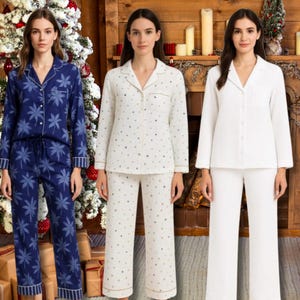 Puede incluir: Se muestran tres conjuntos de pijamas. Uno es azul marino con un estampado floral blanco, otro es blanco roto con un estampado de estrellas doradas, y el tercero es blanco liso. Cada conjunto incluye una camisa con botones y pantalones.
