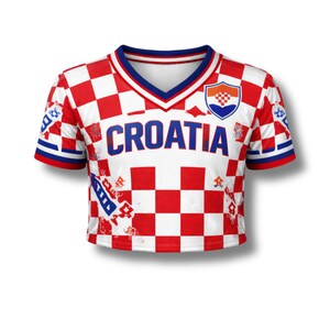 May include: A cropped white and red checkered Croatia soccer jersey with the word "CROATIA" in blue block letters across the chest. The jersey has a V-neck with blue trim and a Croatian coat of arms on the upper right chest.