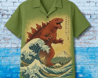 May include: Green short-sleeved button-up shirt featuring a Godzilla graphic in the style of Hokusai's "The Great Wave off Kanagawa." The graphic includes a red Godzilla, a large wave, and a mountain. Japanese text is also present.