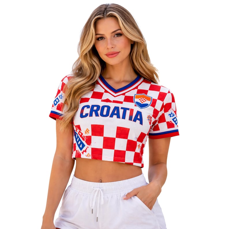 May include: Cropped white and red checkered Croatia soccer jersey with a blue V-neck collar and the word "CROATIA" across the chest. The jersey features the Croatian coat of arms and is worn with white shorts.