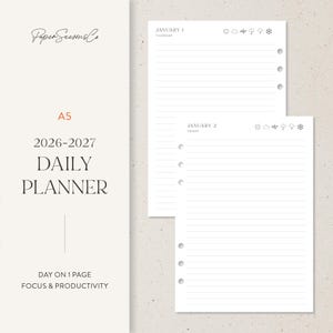 Peut inclure: Un agenda quotidien A5 pour 2026-2027 avec des pages lignées. L'agenda comprend le texte "Paper Seasons Co", "DAILY PLANNER" et "DAY ON 1 PAGE FOCUS & PRODUCTIVITY". Les pages sont blanches avec des lignes grises et des icônes météo.