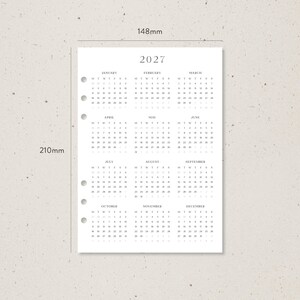 K&ouml;nnte beinhalten: A5-Kalendereinlage f&uuml;r 2027, misst 14,8 cm x 21 cm, mit minimalistischem Design. Der Kalender hat ein einfaches Layout mit dem Jahr oben und den Monaten darunter. Das Papier ist f&uuml;r einen Ordner vorgestanzt.