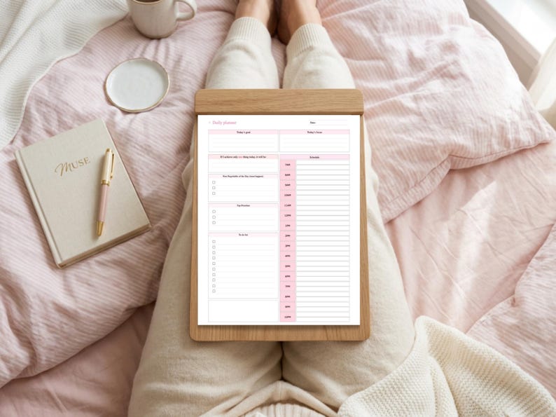 Pu&ograve; includere: Un foglio di pianificazione giornaliera su una cartellina in legno con sfondo bianco e intestazioni e linee rosa. Il testo include Daily planner, Date, Today's goal, Today's focus, 10 positive tasks, Schedule, Top Priorities e To do list.