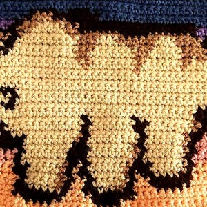 May include: A handmade crochet blanket featuring a large, tan-colored cartoon character with dark brown outlines. The background transitions from orange to purple and blue, resembling a sunset. The blanket is made of soft yarn.