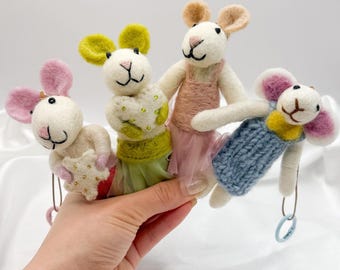 May include: Four handmade felt mice dolls with pink, yellow, and beige ears and outfits. Each mouse has a unique outfit, including a pink dress, a blue sweater, and a green skirt. The dolls are held by a hand.