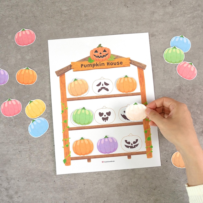 May include: A printable activity sheet titled Pumpkin House featuring a wooden structure with three shelves. The sheet includes various colorful pumpkin cutouts in shades of orange, green, purple, yellow, and blue, along with ghost-like pumpkin faces.