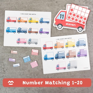Puede incluir: Juego educativo de emparejamiento de números con ilustraciones de camiones coloridos. El juego incluye tarjetas con los números del 1 al 20 y patrones de puntos correspondientes. El texto "I Can Count and Match" se muestra en las tarjetas.