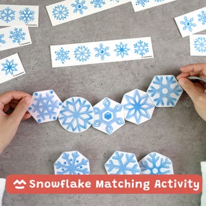 May include: A snowflake matching activity set featuring various paper cutouts of blue snowflakes in hexagonal and circular shapes, with additional strips and individual pieces displaying snowflake illustrations on a gray surface.