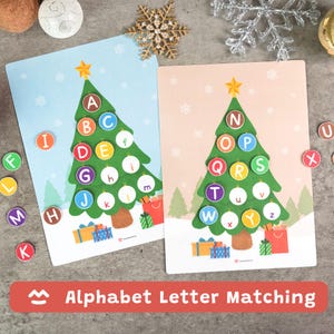 May include: Two educational alphabet letter matching boards with Christmas tree designs. Each tree has colorful letters, with matching letter tiles scattered around. The boards are on a light gray surface with decorative snowflakes.