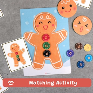 Puede incluir: Juego de actividades de emparejamiento de hombre de jengibre. El conjunto incluye un recorte grande de hombre de jengibre con botones coloridos, tarjetas de emparejamiento y recortes de caras redondas. El fondo es azul claro con copos de nieve. El texto "Matching Activity" está en una pancarta roja.