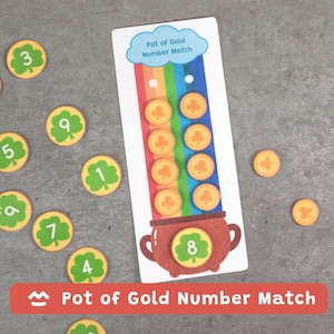 May include: A children's educational game titled "Pot of Gold Number Match". The game features a white card with a rainbow, gold coins, and a pot of gold. Several circular tokens with numbers and shamrocks are scattered around the card.