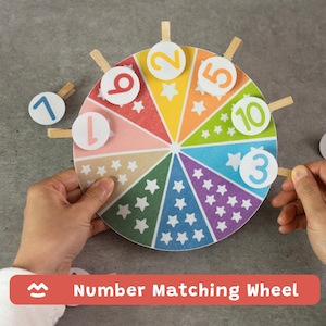 Puede incluir: Una colorida rueda de emparejamiento de números con patrones de estrellas. La rueda está dividida en segmentos de diferentes colores y tiene los números del 1 al 10. El texto "Number Matching Wheel" se muestra en la parte inferior.