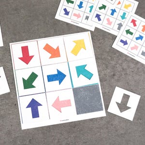 May include: A set of colorful arrow-shaped cutouts on white squares, arranged in a grid. Additional cards with various arrow patterns are scattered around. The arrows are in shades of red, orange, yellow, green, blue, and pink.