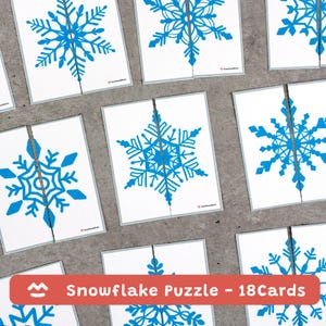 Pode incluir: Cartões brancos com desenhos de flocos de neve azuis, cada um cortado ao meio. O texto "Snowflake Puzzle - 18 Cards" é exibido em uma faixa vermelha. Os flocos de neve são detalhados e simétricos.