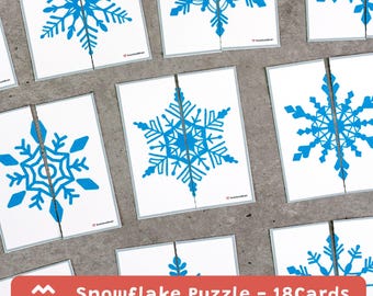 May include: A collection of white cards with blue snowflake designs, each cut in half. The text "Snowflake Puzzle - 18 Cards" is displayed on a red banner at the bottom. The snowflakes are detailed and symmetrical.