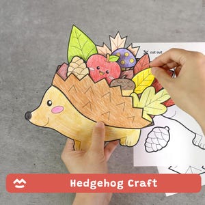 May include: A paper craft project featuring a colored-in hedgehog with a brown back, carrying a collection of autumn items including a red apple with a face, a pinecone, an acorn, and various green, yellow, and orange leaves on its back.
