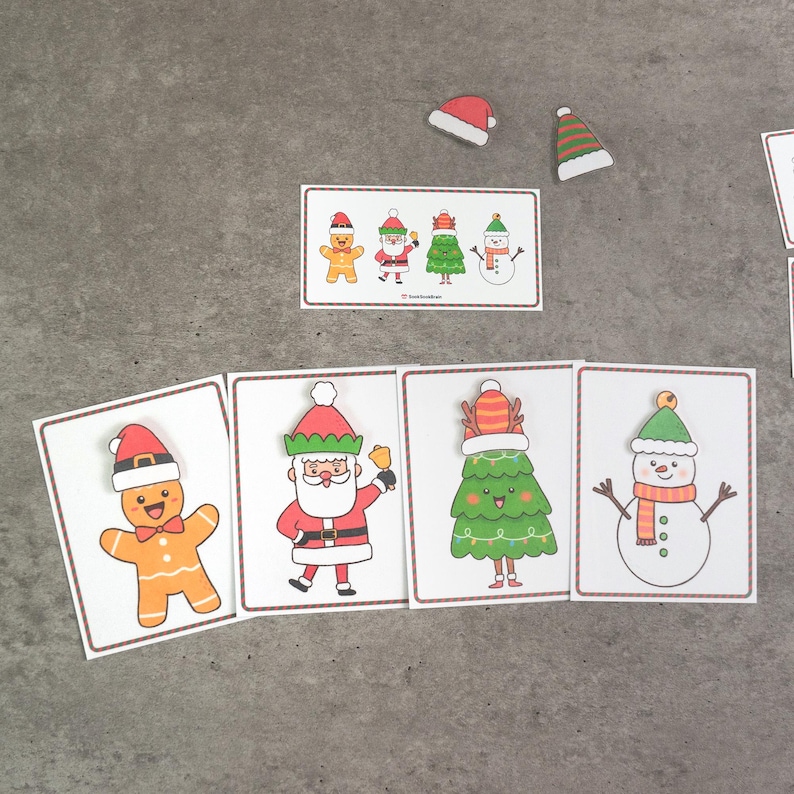 Puede incluir: Tarjetas navide&ntilde;as con ilustraciones festivas de un hombre de jengibre, Pap&aacute; Noel, un &aacute;rbol de Navidad y un mu&ntilde;eco de nieve. Cada tarjeta tiene un borde blanco. Tarjetas y gorros de Pap&aacute; Noel adicionales est&aacute;n dispersos.