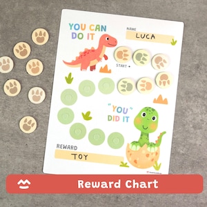 May include: A white reward chart with a dinosaur theme. The chart features a red dinosaur, a green dinosaur hatching from an egg, and paw print tokens. The text includes "You Can Do It", "You Did It", and "Reward Toy".