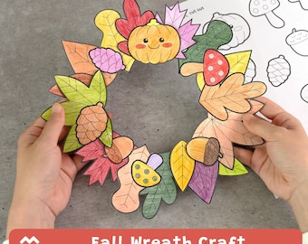 May include: A paper craft wreath featuring colored illustrations of autumn leaves, a smiling pumpkin, mushrooms, and pinecones. The wreath is circular with a central opening. A separate sheet of paper with black and white line art is visible.