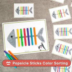 Puede incluir: Actividad educativa de clasificación de colores con ilustraciones de espinas de pescado y ranuras para palitos de helado de colores. El conjunto incluye varias tarjetas y palitos de varios colores. El texto "Popsicle Sticks Color Sorting" es visible.