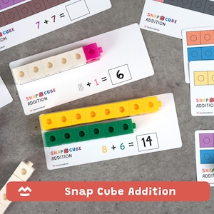 Op de afbeelding: Educatief rekenspel met witte kaarten met optelsommen en kleurrijke snap cubes. De kaarten tonen vergelijkingen zoals 5 + 1 = 6 en 8 + 6 = 14. Het spel is ontworpen om optellen te leren.