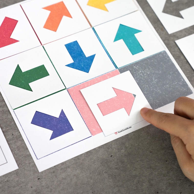 May include: A set of colorful arrow cards on a gray surface. The cards feature arrows in various colors, including red, orange, green, blue, and pink. A hand is pointing at a pink arrow card. The text "SookSookBrain" is visible.