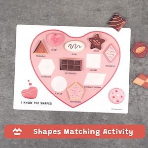 May include: A white wooden shapes matching activity board with a pink heart-shaped cutout. The board features various shapes like a triangle, heart, oval, star, and rectangle. The text "I KNOW THE SHAPES" is printed on the board. The bottom of the board reads "Shapes Matching Activity".