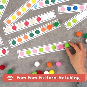 Puede incluir: Un conjunto de actividades educativas Pom Pom Pattern Matching que presenta múltiples tiras rectangulares blancas con círculos de colores impresos. Las tiras contienen secuencias de pompones difusos rojos, naranjas, amarillos, verdes, rosas y blancos.