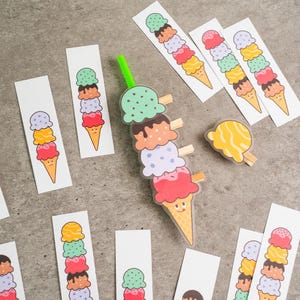 May include: A collection of colorful ice cream cone-shaped bookmarks and a decorative ice cream cone with wooden clips. The bookmarks feature stacked scoops of ice cream in various colors, including green, brown, pink, and yellow.