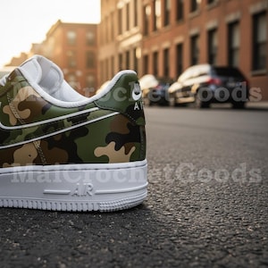 May include: A close-up of a camouflage-patterned sneaker with a white sole. The shoe features a green, brown, and tan camouflage design with a white swoosh and trim. The word "AIR" is visible on the sole.
