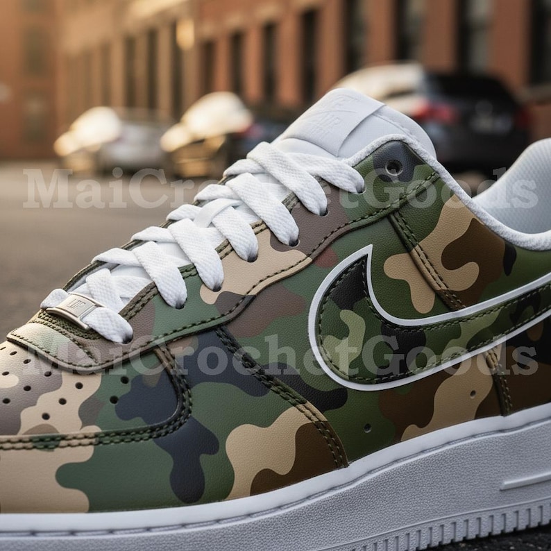 May include: A close-up of a camouflage-patterned sneaker. The shoe features a white sole, white laces, and a white Nike swoosh. The camouflage design incorporates shades of green, brown, and black. The text "MaiCrochet Goods" is visible.
