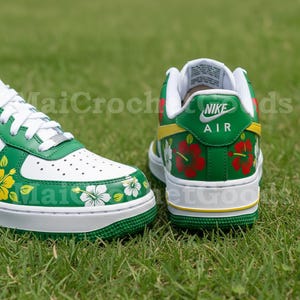 Puede incluir: Zapatillas Nike Air Force 1 blancas y verdes con dise&ntilde;os florales. Las zapatillas presentan una base blanca con detalles verdes, una suela verde y patrones de flores rojas y blancas. El logotipo de Nike Air es visible.