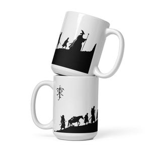 May include: Two white ceramic mugs stacked on top of each other. Each mug features a black silhouette design. One mug depicts a wizard with a staff, and the other shows figures walking with a horse. The mugs have a curved handle.
