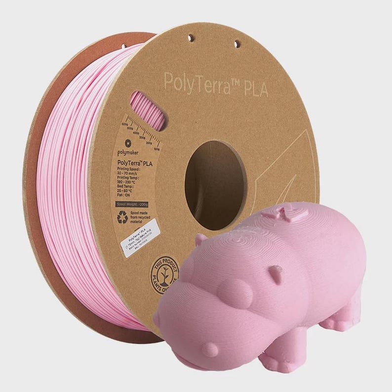 May include: A pink 3D printing filament spool labeled "PolyTerra PLA" next to a 3D-printed pink hippopotamus figurine. The spool is made from recycled materials. The hippo has a textured surface.