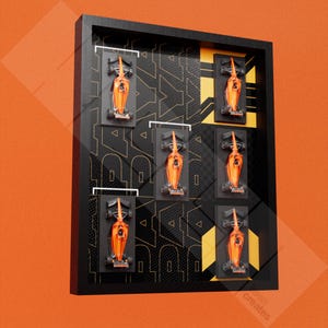 Puede incluir: Un marco negro con un patrón de cuadrícula y acentos amarillos muestra ocho coches de carreras en miniatura de color naranja. Los coches están dispuestos en un patrón de cuadrícula dentro del marco.