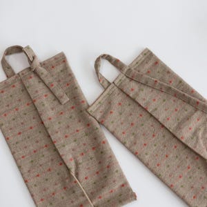 Può includere: Due sacchetti beige in tessuto per bottiglie di vino con manici. Le borse presentano un motivo ripetuto di punti rossi e verdi collegati da sottili linee rosse. Una borsa ha una chiusura a cinturino, su sfondo bianco.