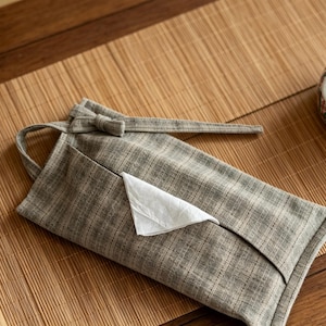 Può includere: Un porta fazzoletti grigio con un fazzoletto bianco, un contenitore in ceramica decorativo con motivi floreali rossi e verdi e una piccola ciotola. Gli oggetti sono su un tappetino di bambù e un tavolo di legno.