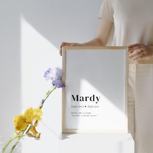 Könnte beinhalten: Ein gerahmter Druck mit dem Wort "Mardy" in fetter Schrift, zusammen mit seiner Aussprache und Definition. Der Rahmen ist aus hellem Holz. Links vom Druck befindet sich eine Vase mit gelben und lila Blumen.