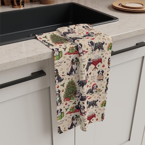 May include: A beige kitchen towel featuring a repeating pattern of Bernese Mountain Dogs in various holiday scenes, including Christmas trees, wrapped gifts, and festive lights. The text includes phrases like Santa Paws, Ho Ho Woof, and I didn't do it.