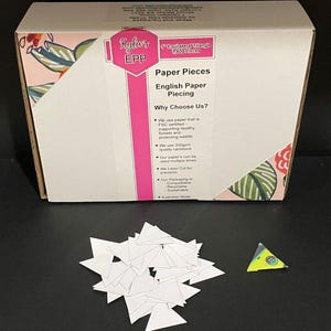 May include: A box containing 1,600 white equilateral triangle paper pieces for English paper piecing. The box is pink and white with a floral design and the text "Kyler's EPP Paper Pieces English Paper Piecing Why Choose Us?" The box is on a white surface with a pile of white triangles and a single green, yellow, and blue triangle.