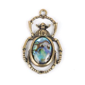 Puede incluir: Un colgante de metal dorado en forma de escarabajo con una incrustación de nácar de abulón iridiscente.