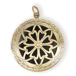 May include: A gold-toned metal locket with a circular design featuring a black flower with intricate cutouts. The locket has a loop at the top for attaching a chain.