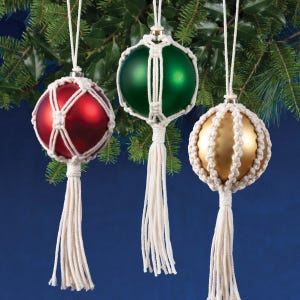 May include: Three Christmas ornaments with macrame covers. The ornaments are red, green, and gold. Each ornament has a white tassel.