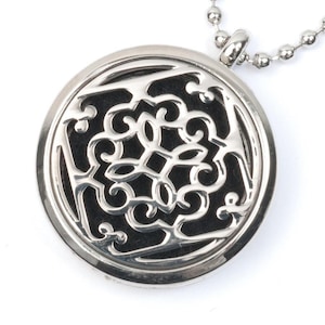 May include: A silver pendant necklace with a round, openwork design. The pendant features a black, intricate floral pattern.