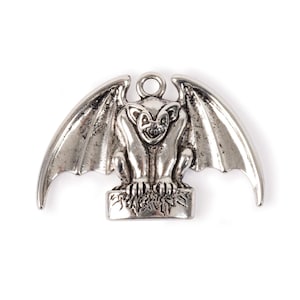 May include: Silver gargoyle charm with wings, sitting on a stone base. The gargoyle has a menacing expression with sharp teeth and claws.