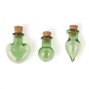 May include: Three small glass bottles with cork stoppers. The bottles are green and have different shapes: heart, round, and teardrop.