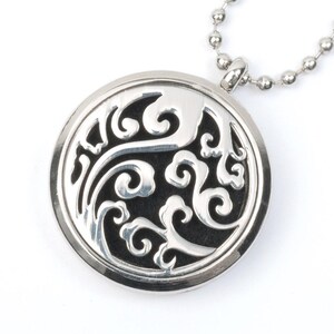 Puede incluir: Collar con colgante redondo de plata, con un diseño calado en forma de espirales. El colgante está unido a una cadena de plata.