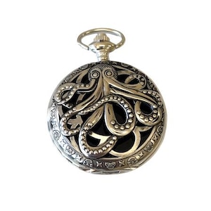 May include: Silver-toned pocket watch with an intricate octopus design. The watch features a detailed, openwork design of an octopus on the front, with a circular shape and a loop at the top for a chain. The background is black.